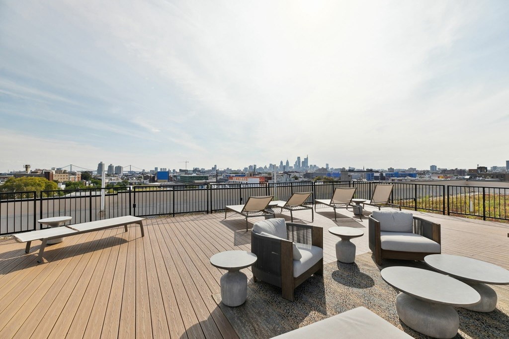 A wooden deck with several chairs and tables overlooking a city skyline.