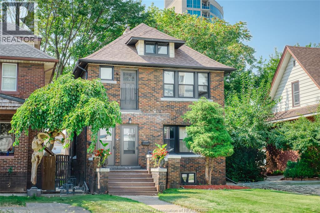 A brick house with a porch and a tree in front.