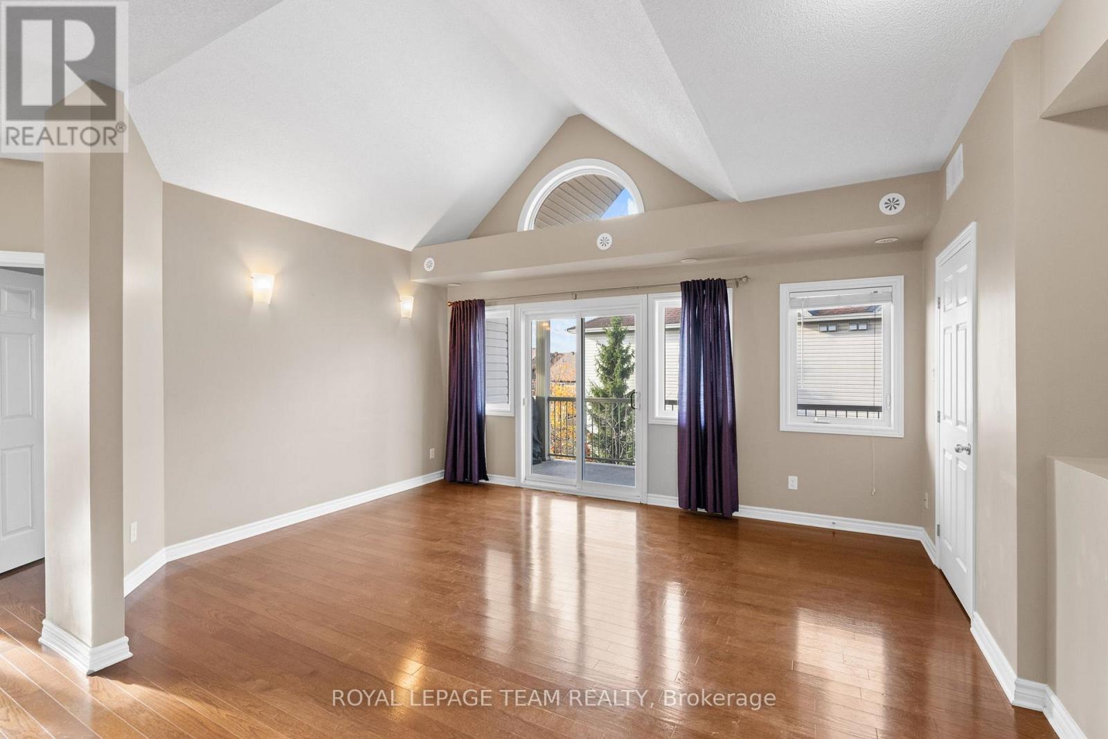A spacious room with wood flooring and a large window with curtains.
