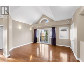 A spacious room with wood flooring and a large window with curtains.
