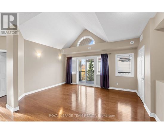 A spacious room with wood flooring and a large window with curtains.