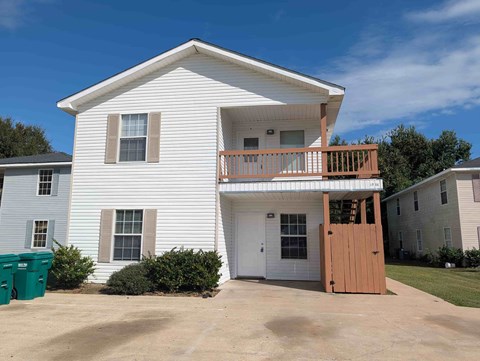 A white house with a brown door and a balcony.