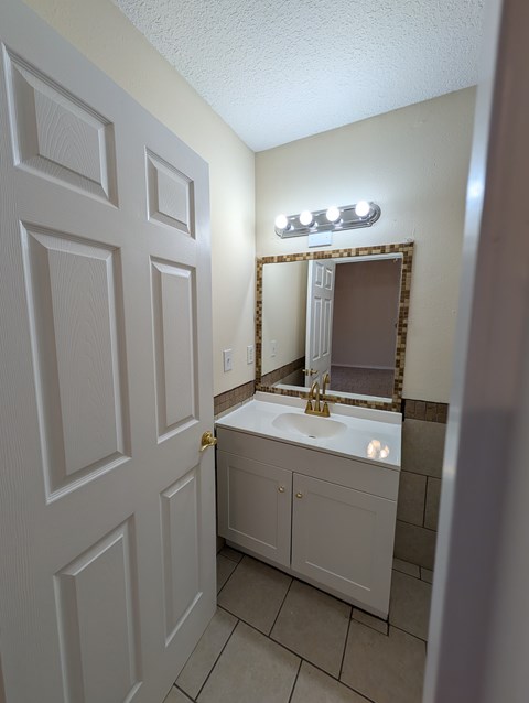 A white bathroom with a sink, mirror, and light switch.