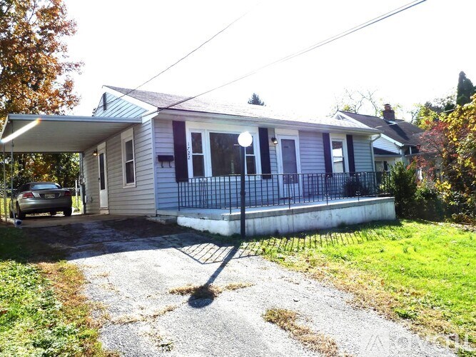 A house with a white fence and a tree with orange leaves in front of it.