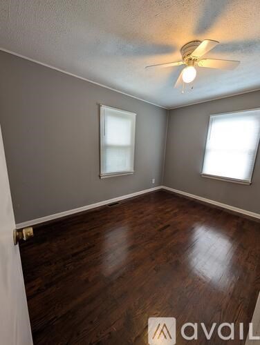 A room with a ceiling fan and two windows.