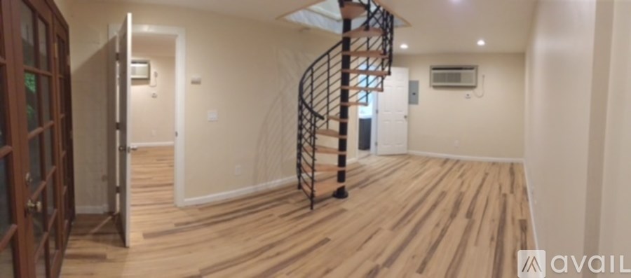 A spacious room with wooden flooring and a spiral staircase.