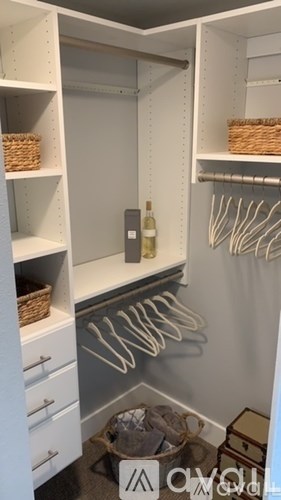 A white closet with a basket on the shelf and clothes hanging on the rack.