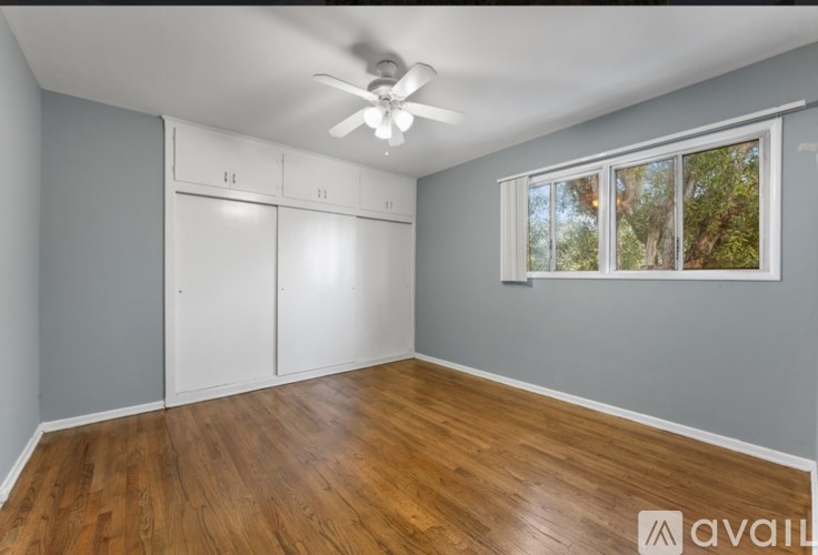 A room with a ceiling fan and a window showing trees outside.