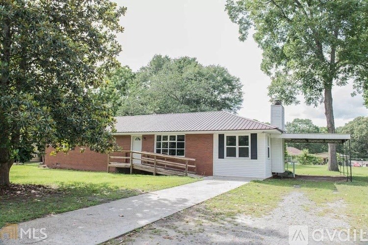 A house with a red brick exterior and a white garage door is surrounded by trees.