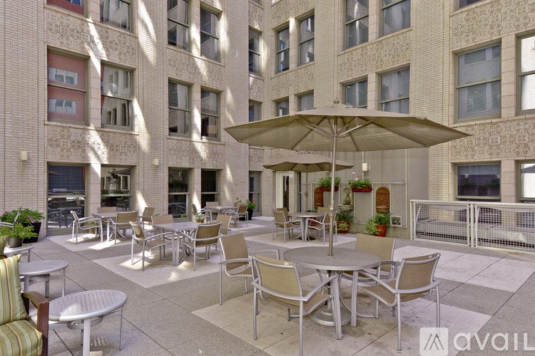 A patio with chairs and tables is shaded by a large umbrella.