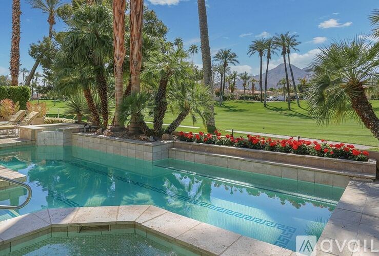 A pool surrounded by palm trees and red flowers.