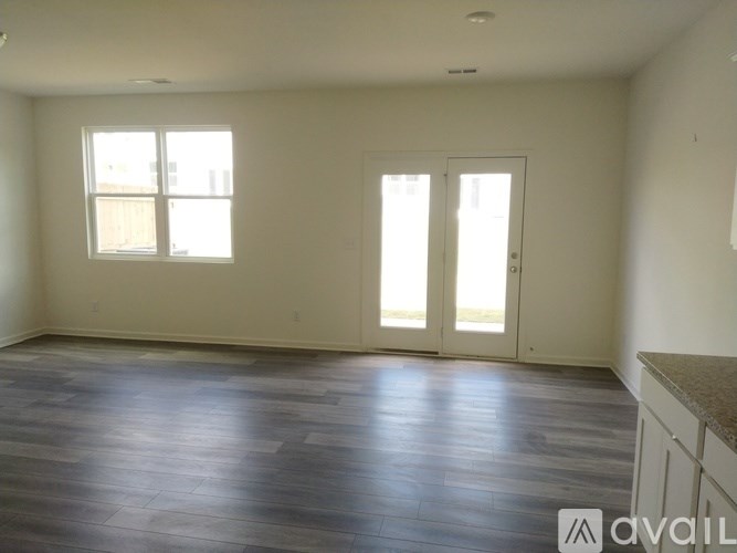 A spacious room with wood flooring and two windows.