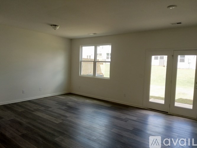 A spacious room with wood flooring and two windows.