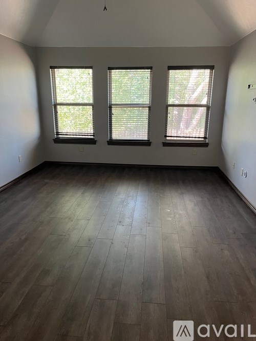 A room with wooden flooring and three windows.