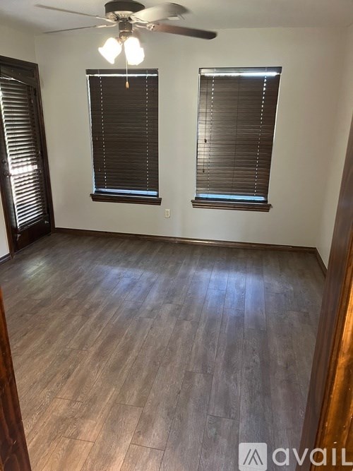 A room with wooden flooring and two windows with blinds.