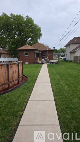 A sidewalk leads to a house with a fence and a tree in the background.
