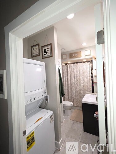 A white fridge is in a narrow hallway with a toilet and sink in the background.