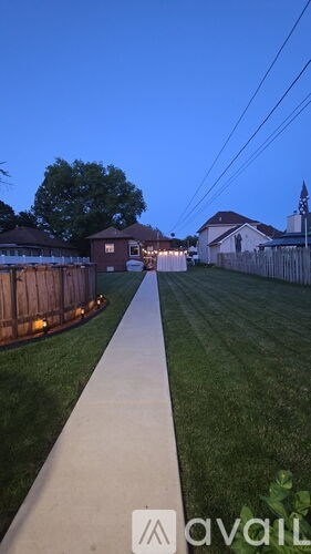 A long concrete pathway leads to a house with a fence and lights on.