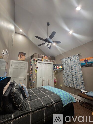 A bedroom with a bed, a ceiling fan, and a wall-mounted TV.