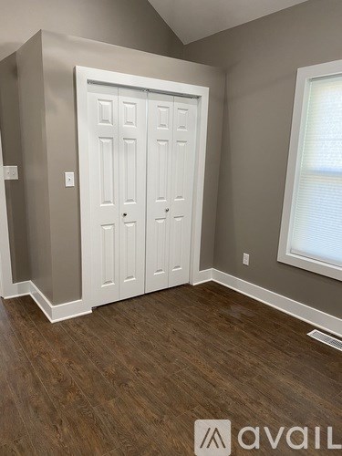 A white door in a room with wooden flooring and a window.