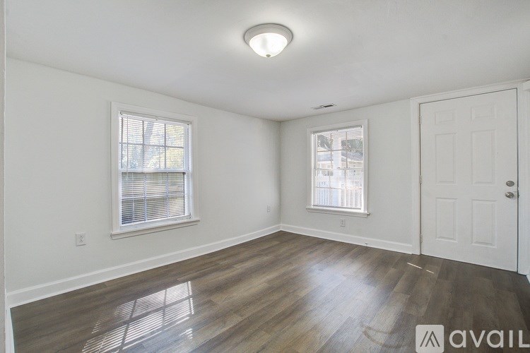 A room with a white door, two windows, and a wooden floor.