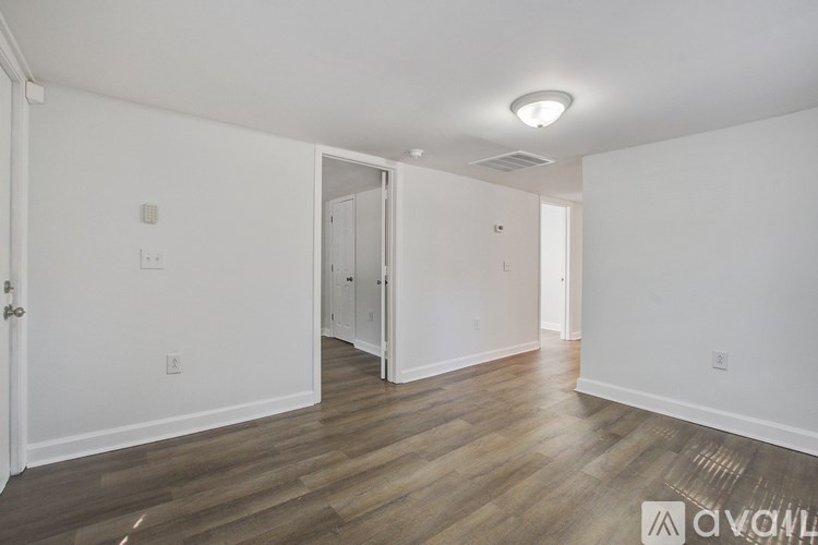 A room with white walls and wooden flooring with a doorway leading to another room.