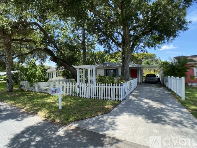 A white picket fence surrounds a house with a red door.