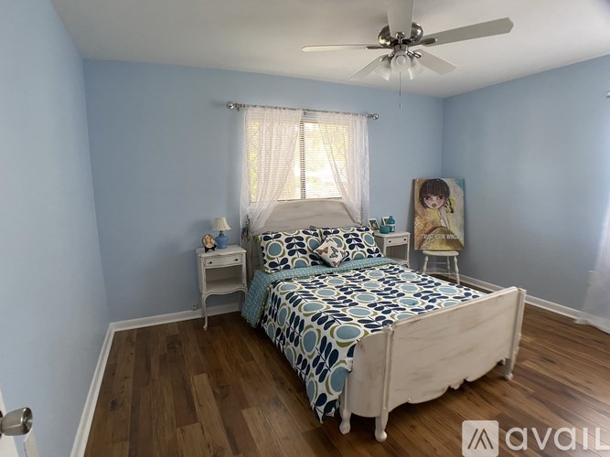 A bedroom with a bed, nightstand, and a painting of a girl on the wall.