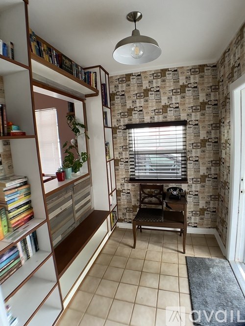 A room with a bookshelf, a window with blinds, and a chair.