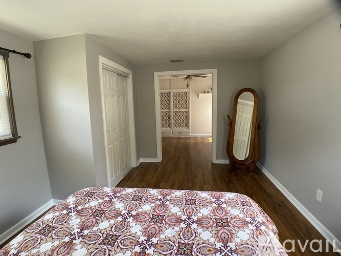 A bedroom with a bed, dresser, mirror, and a doorway leading to another room.