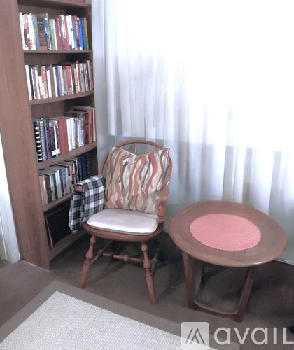 A chair with a plaid pillow sits in front of a bookshelf.