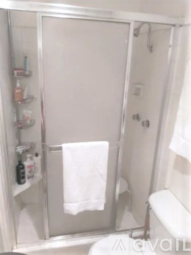 A white bathroom with a towel hanging on the shower door.