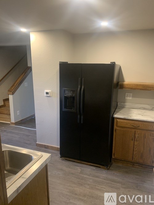 A black fridge in a kitchen with a sink and wooden cabinets.