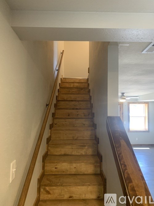 A wooden staircase with a railing on the left side and a window on the right side.