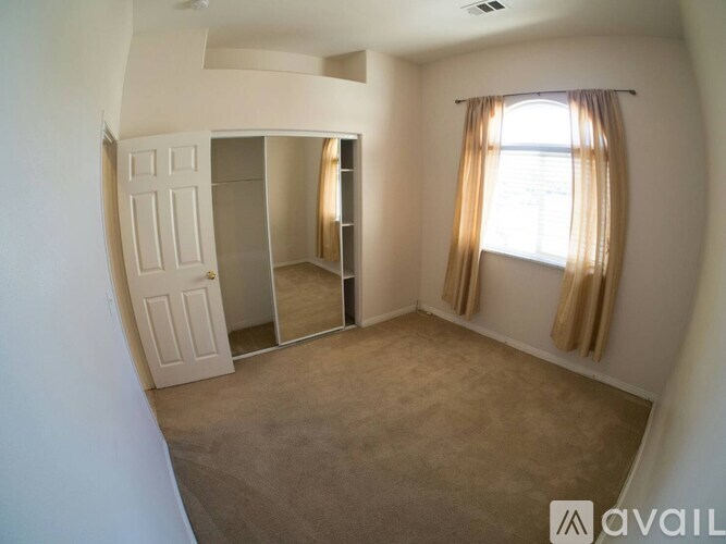 A room with a carpeted floor, a window with curtains, and a sliding door.