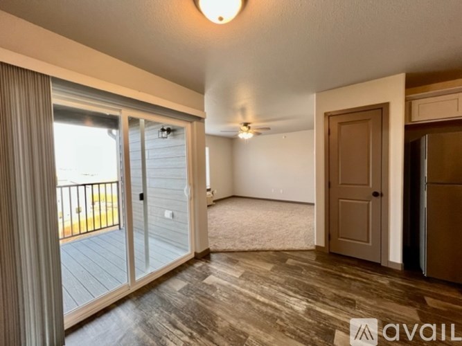 A room with a sliding glass door leading to a balcony, a ceiling fan, and a carpeted floor.