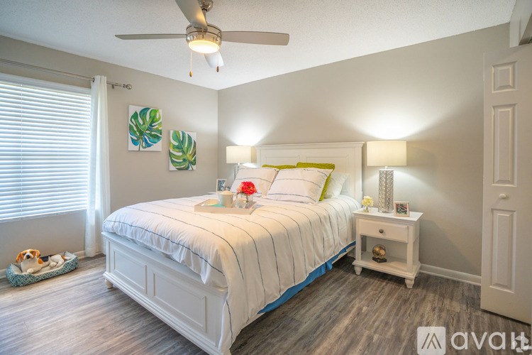 A bedroom with a white bed, a white nightstand, and a ceiling fan.