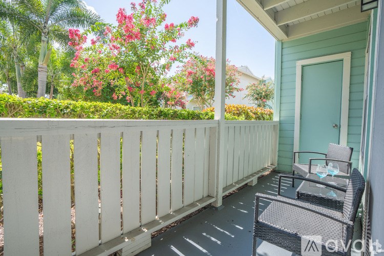 A patio with a white fence and a chair with a table and a bottle on it.