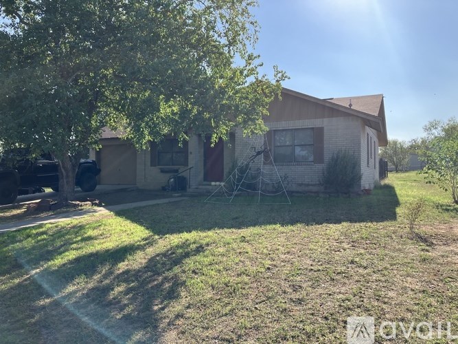 A house with a brown roof and a white fence is surrounded by a grassy area and trees.