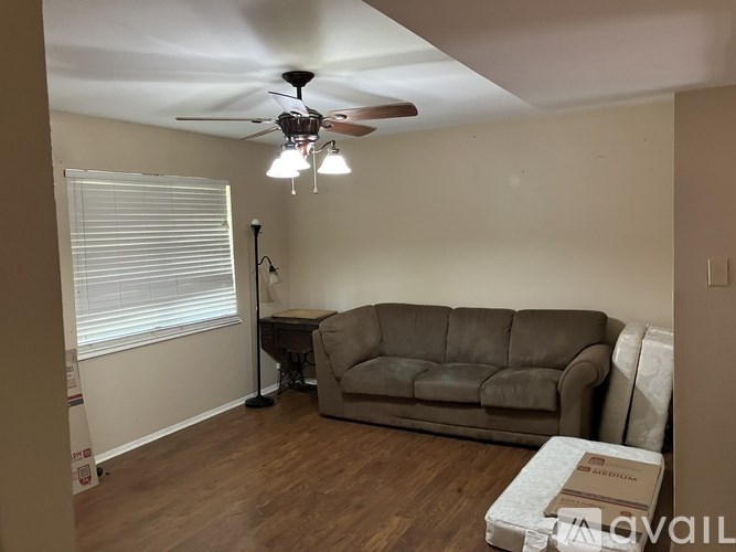 A living room with a couch, a ceiling fan, and a window with blinds.