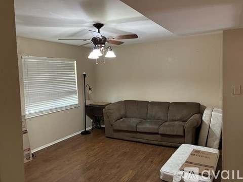 A living room with a couch, a ceiling fan, and a window with blinds.
