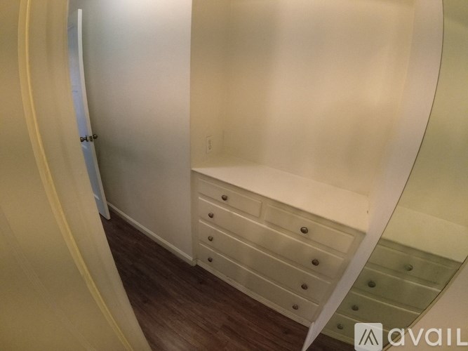 A white circular room with a wooden floor and a white door.