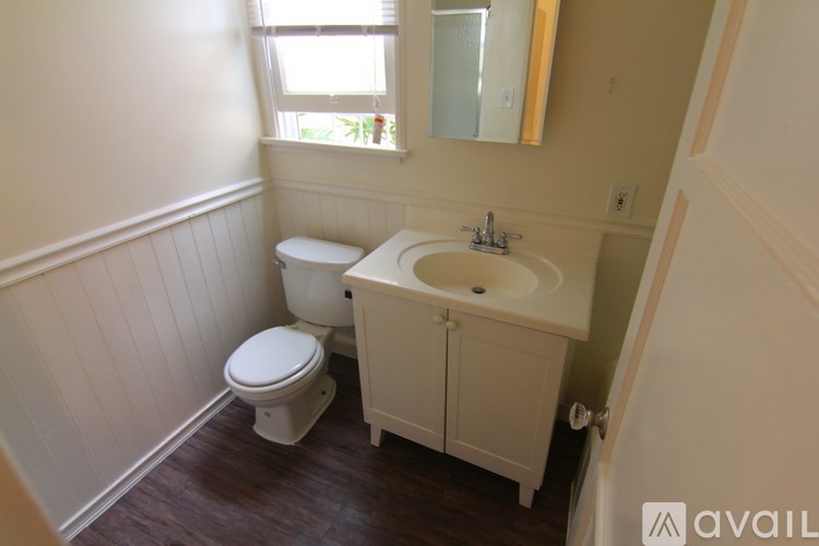 A bathroom with a toilet, sink, and wooden floors.
