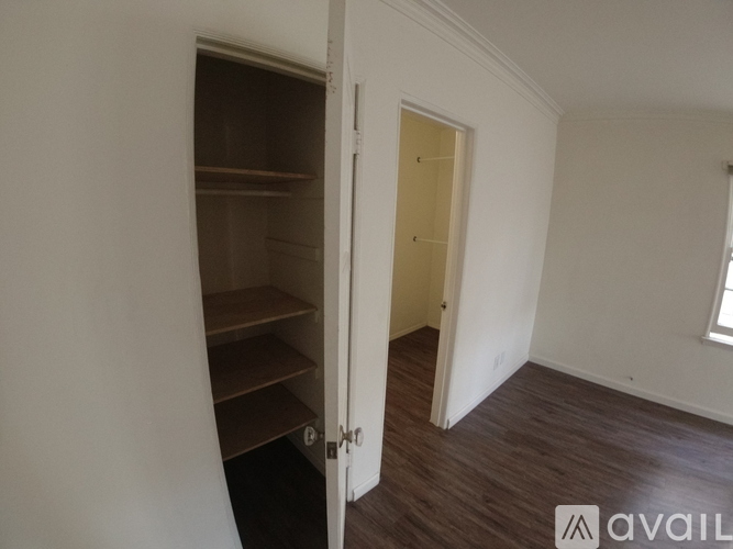 A room with a doorway leading to another room and a shelving unit in the corner.