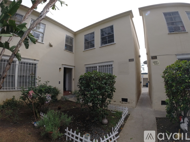A white picket fence separates a small garden from a white building.