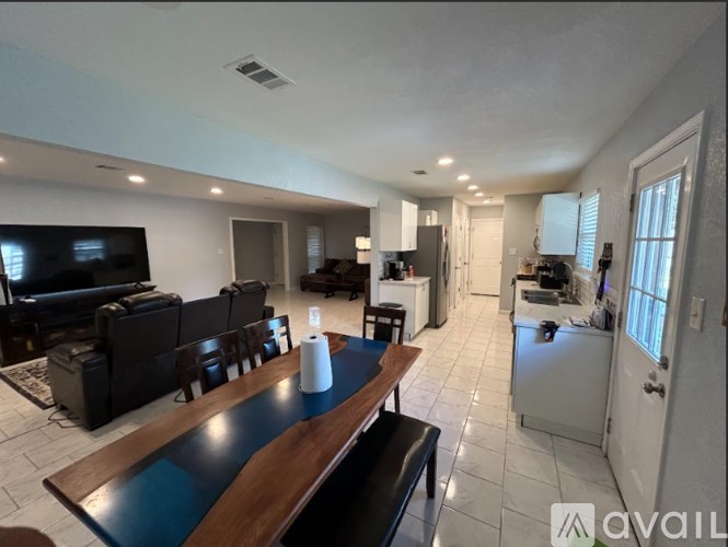 A living room with a television, a dining table, and a kitchen in the background.