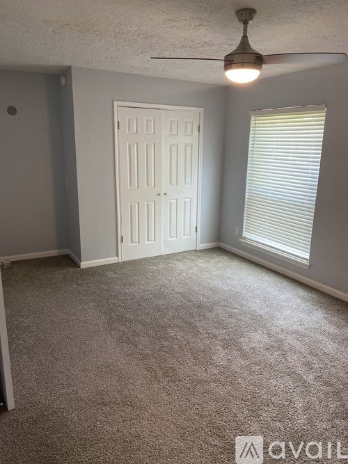 A room with a carpeted floor, a ceiling fan, and a door.