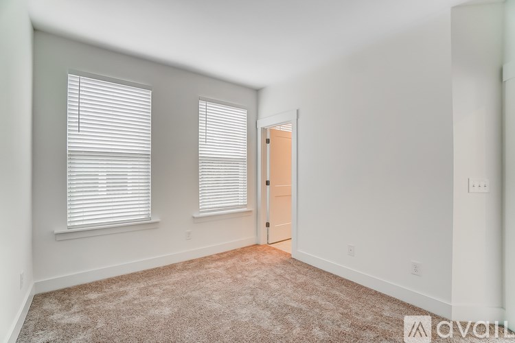 A room with a carpeted floor, a door, and two windows with blinds.