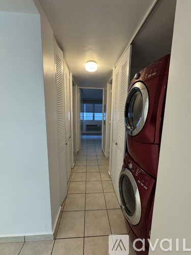 A row of red and white washing machines are lined up in a narrow hallway.