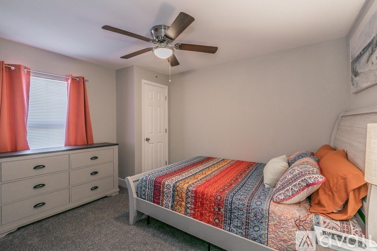 A bedroom with a bed, dresser, and window with red curtains.